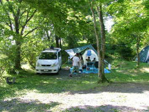 林の中のオートキャンプ場で、マイカーの横にテントを張って過ごしている様子