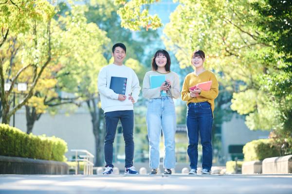 高崎経済大学の学生3人がキャンパスで笑顔で立っている写真